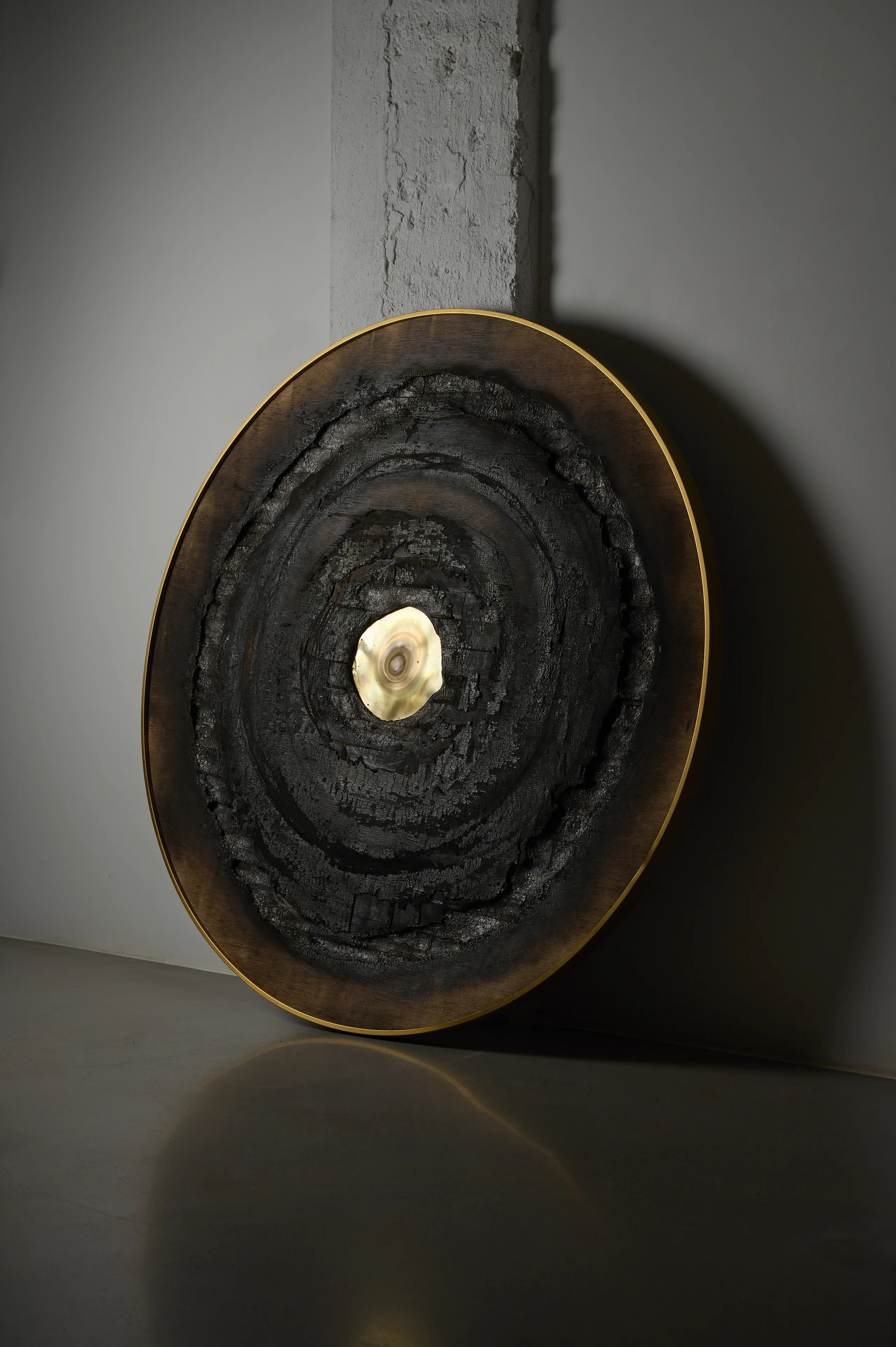 ‘Heliocentrism’ (2021) by Damian Boylan. Circular semi-sculptural painting from his Fire Paintings series, with butane-burned wood, an oxidized brass disc, and a golden frame.