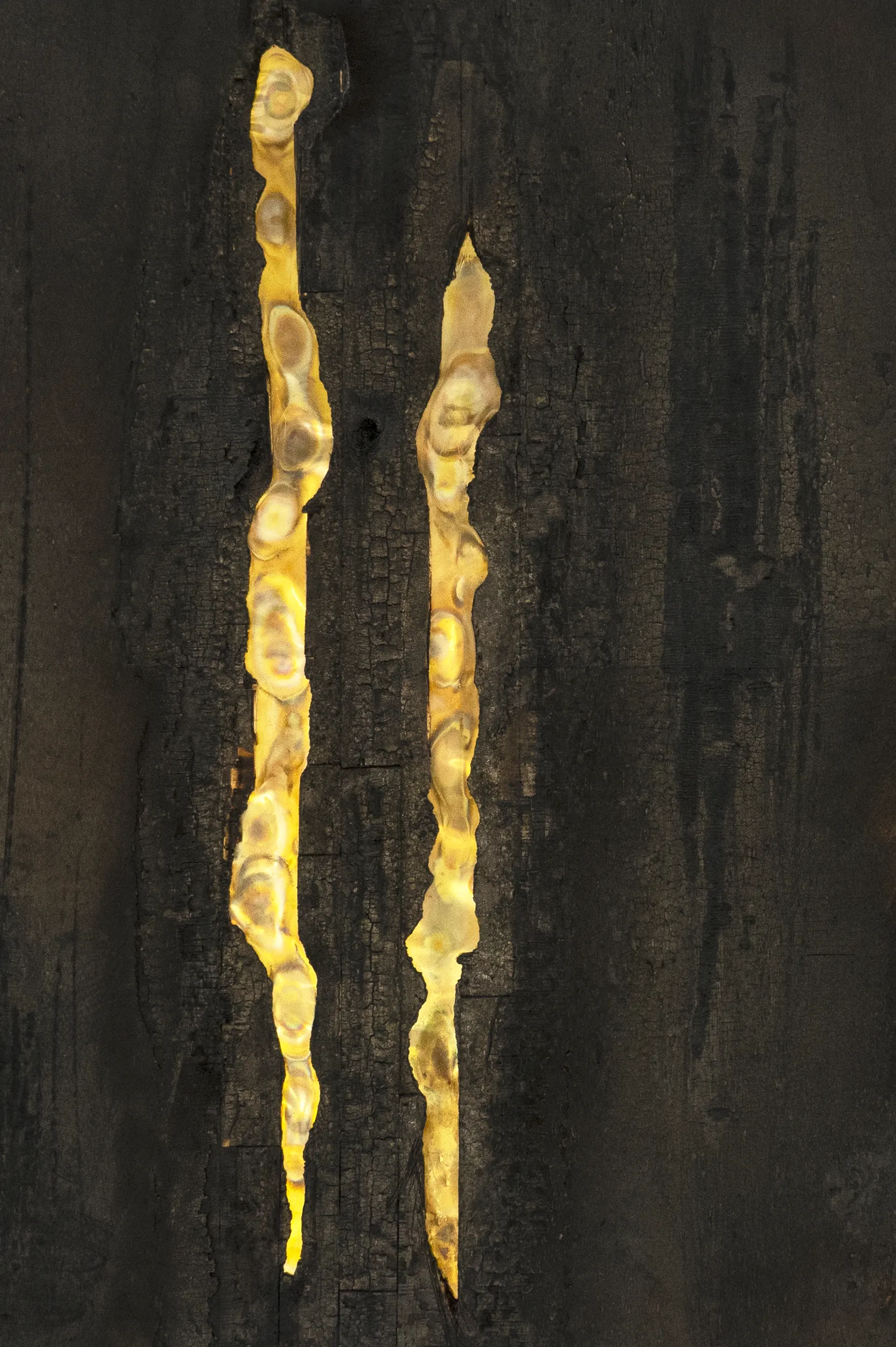 A close up view of the surface details of the artwork 'Parallelism' by artist Damian Boylan from his Fire Paintings series. Black and gold hues are displayed from the artwork's carbonised wood and oxidised brass surface.